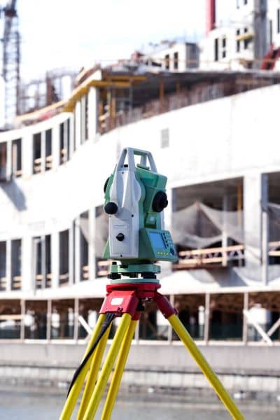 Surveying instrument on tripod capturing precise boundary survey measurements near a canal construction site