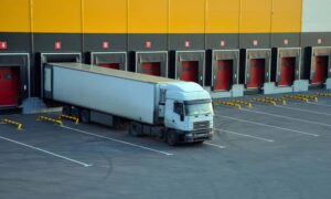 Truck parked at a loading dock with multiple dock doors and marked pavement, showing a work area where a construction staking survey may take place