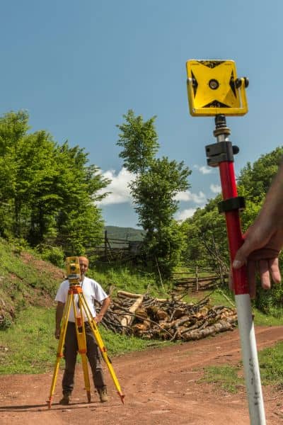 Licensed land surveyor using leveling equipment to measure ground elevation data for FEMA elevation certificate