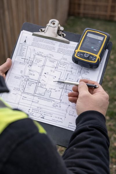 Surveyor reviewing a site plan on a clipboard with GPS device while checking boundary survey measurements on a residential property